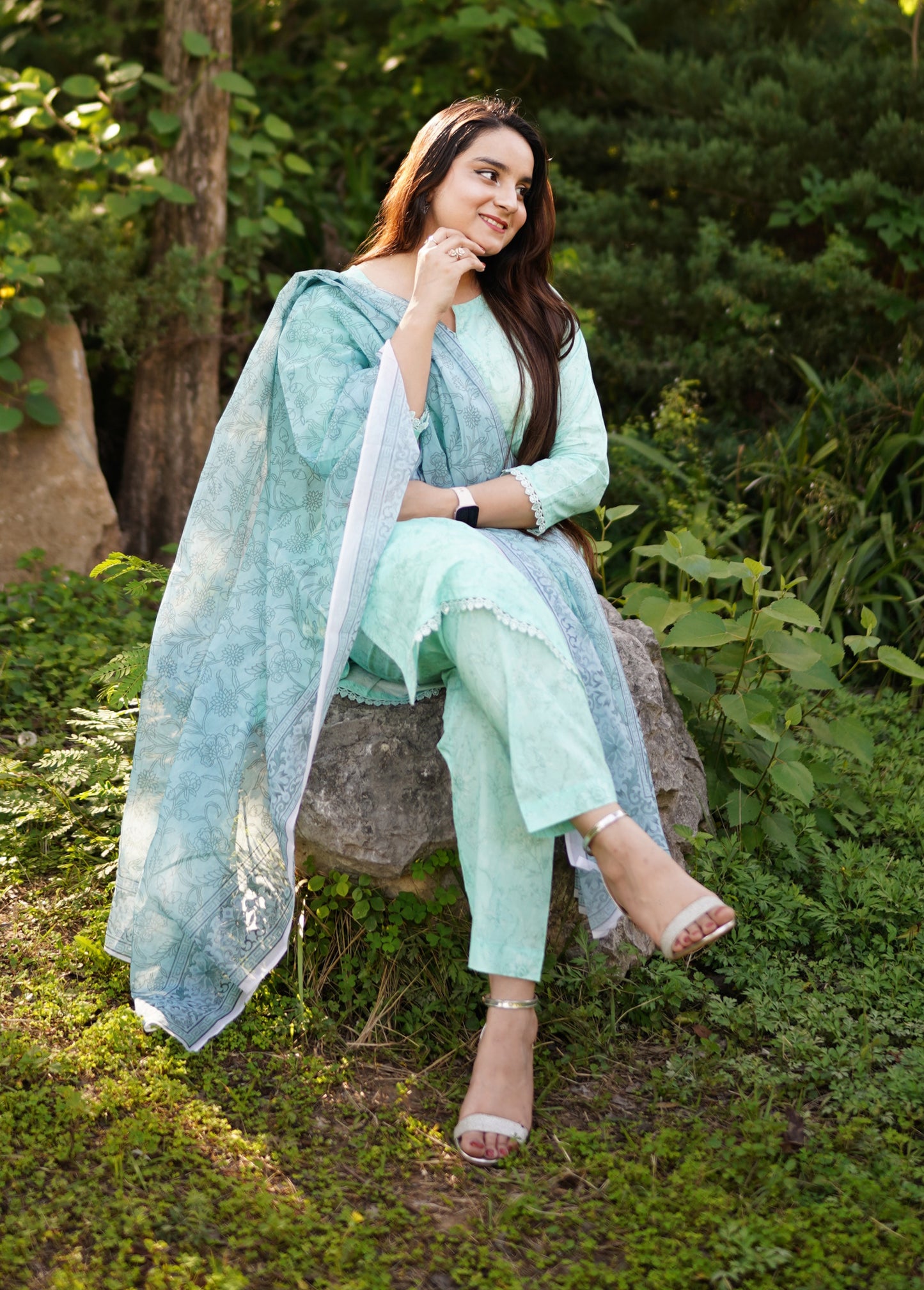Woman in a light green outfit sitting on a stone bench in a garden.