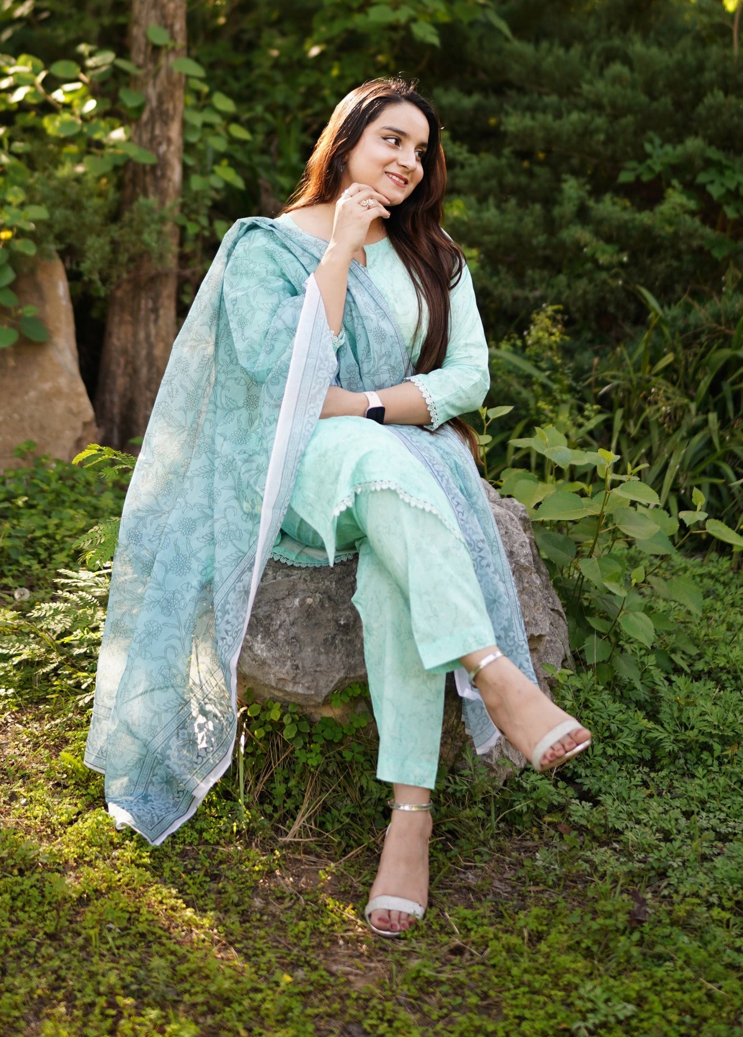 Woman in a light green outfit sitting on a stone bench in a garden.